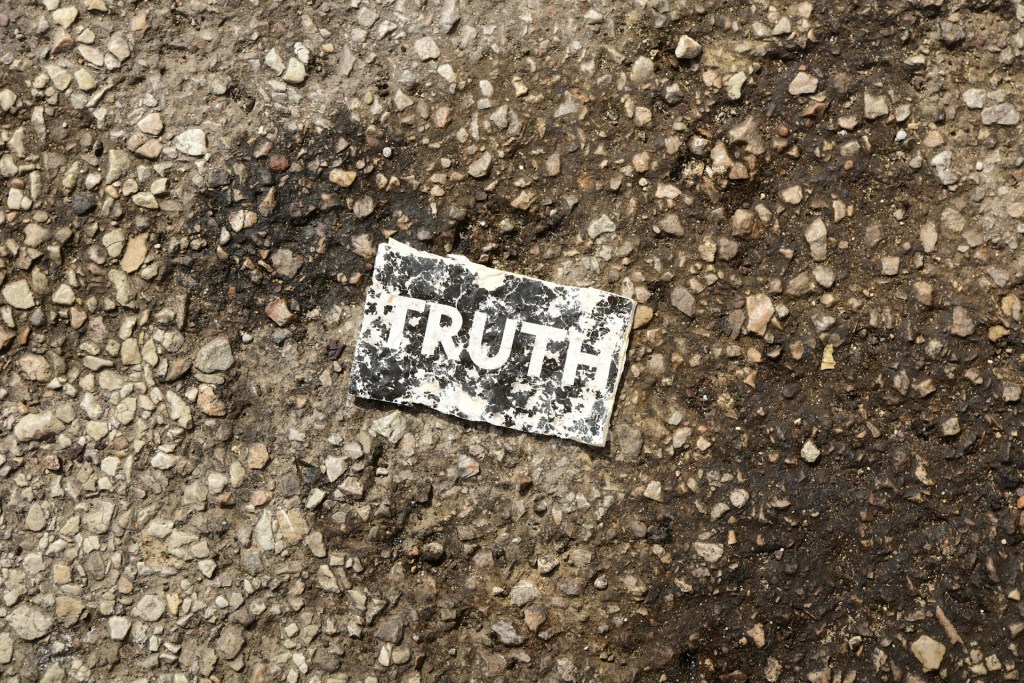 Photo of a damaged card reading "truth" on the backdrop of a gravel parking lot